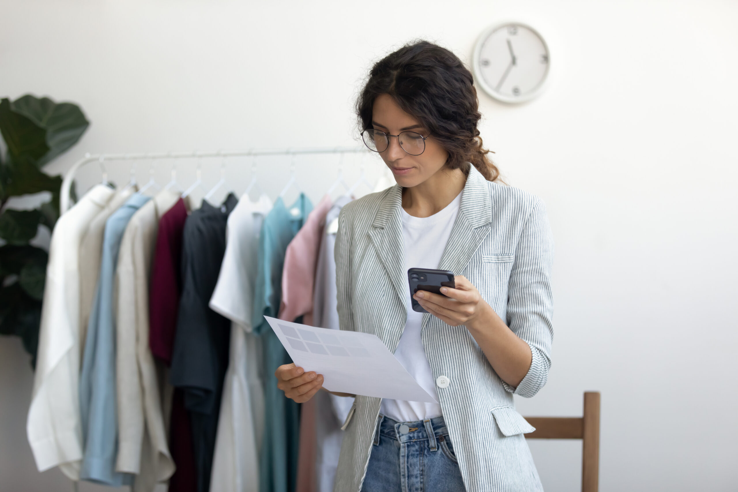 Businesswoman qualified fashion clothing designer selecting fabric samples from catalogue Eine Fachwirtin für Vertrieb checkt die Bestandslisten ihrer Ware anhand einer Liste und des Warenwirtschaftssystems auf dem Handy