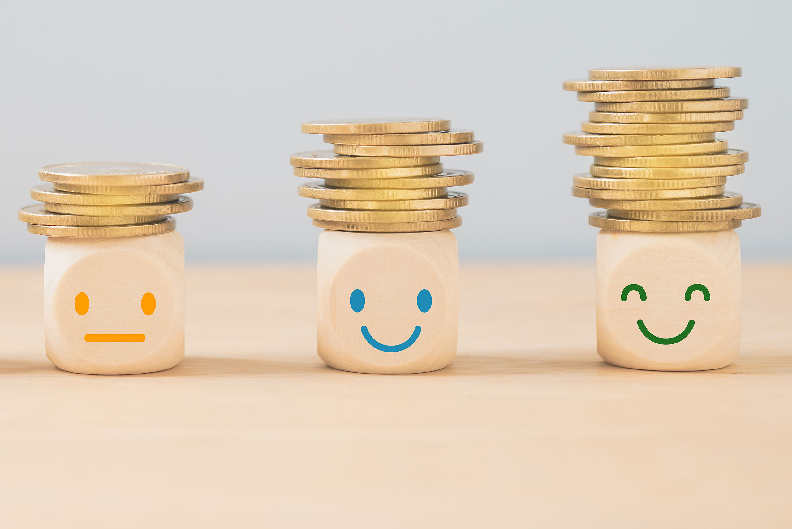 Holzwürfel mit Smiley und Geld. Pro Würfel wird der Smiley freundlicher und es wurde mehr Geld gestapelt.