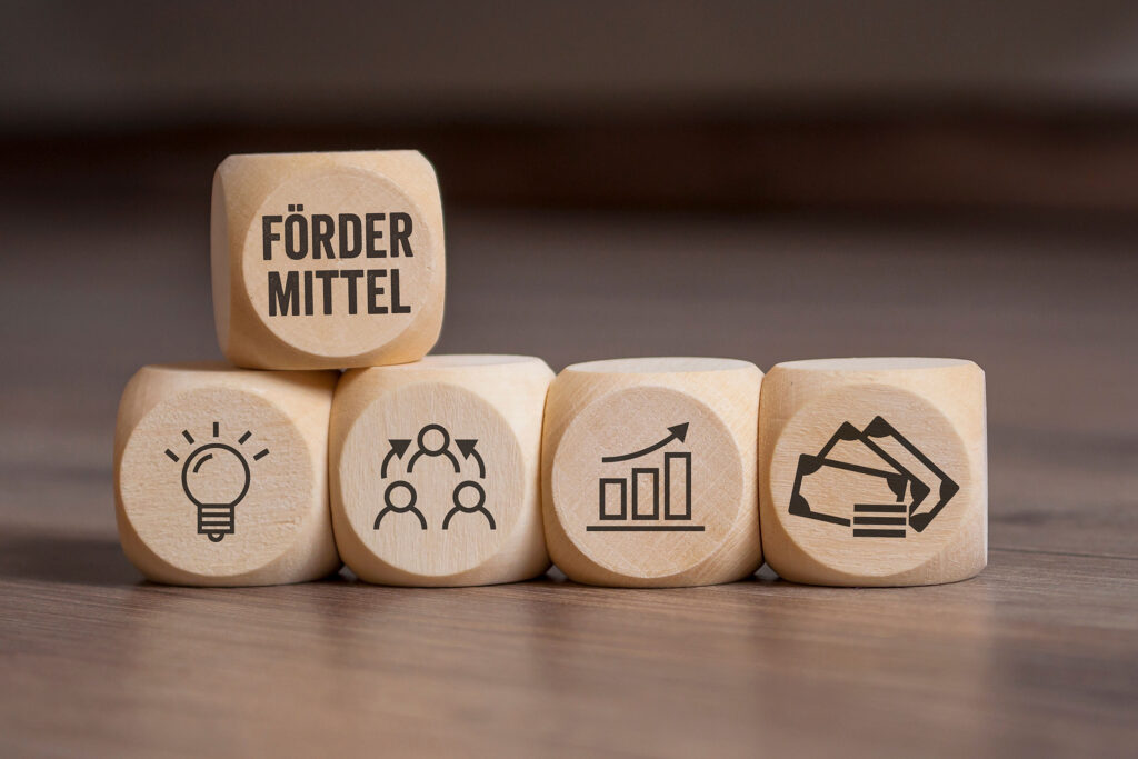 Holzwürfel gestapelt. Auf dem einen Würfel steht Fördermittel.