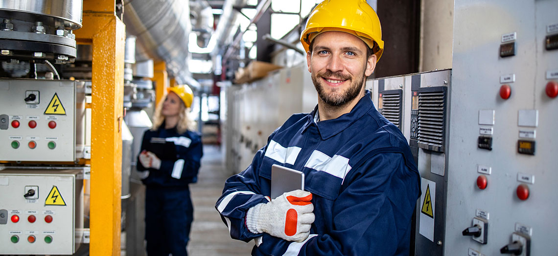 Eine Frau und ein Mann stehen in Arbeitskleidung in einem Schaltraum