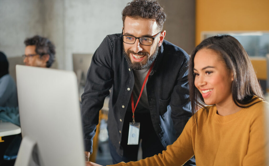 Ein Dozent erklärt einer Studentin etwas am PC.