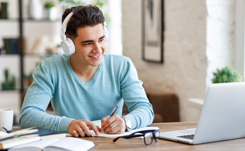 Ein Student sitzt mit Kopfhörern vor dem Laptop und verfolgt ein Online-Seminar.