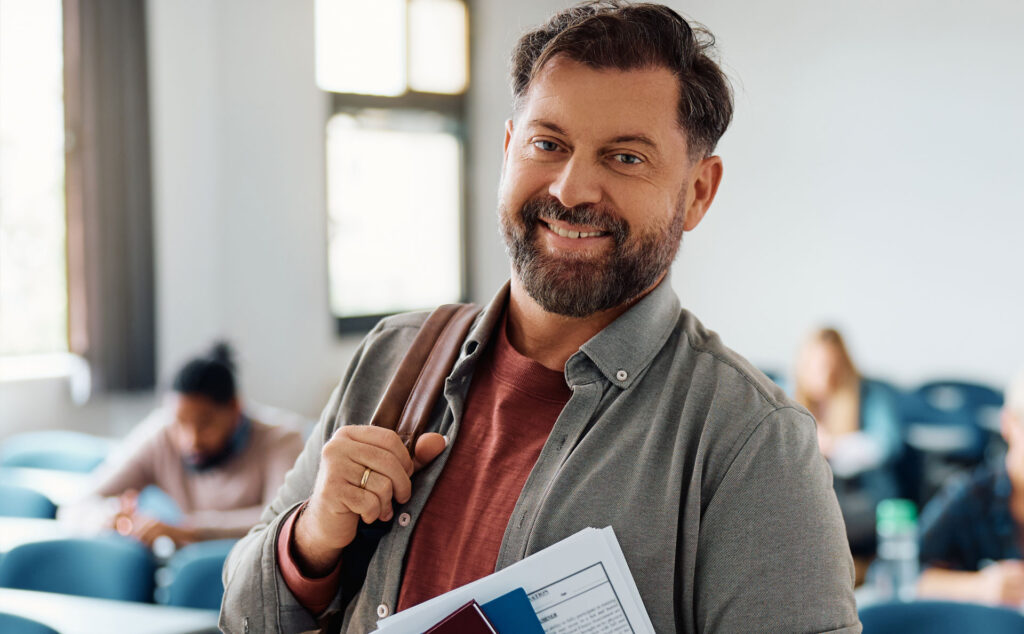 Ein Student steht mit einem Rucksack in einem Schulungsraum und lächelt.