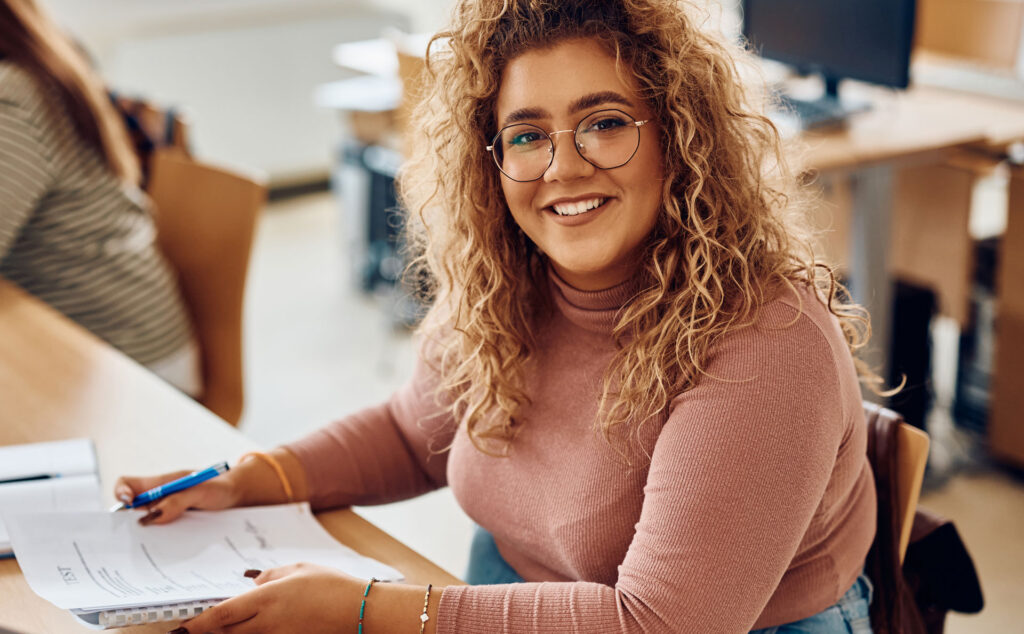 Eine Studentin sitzt am Tisch und hat ein Heft in der Hand.