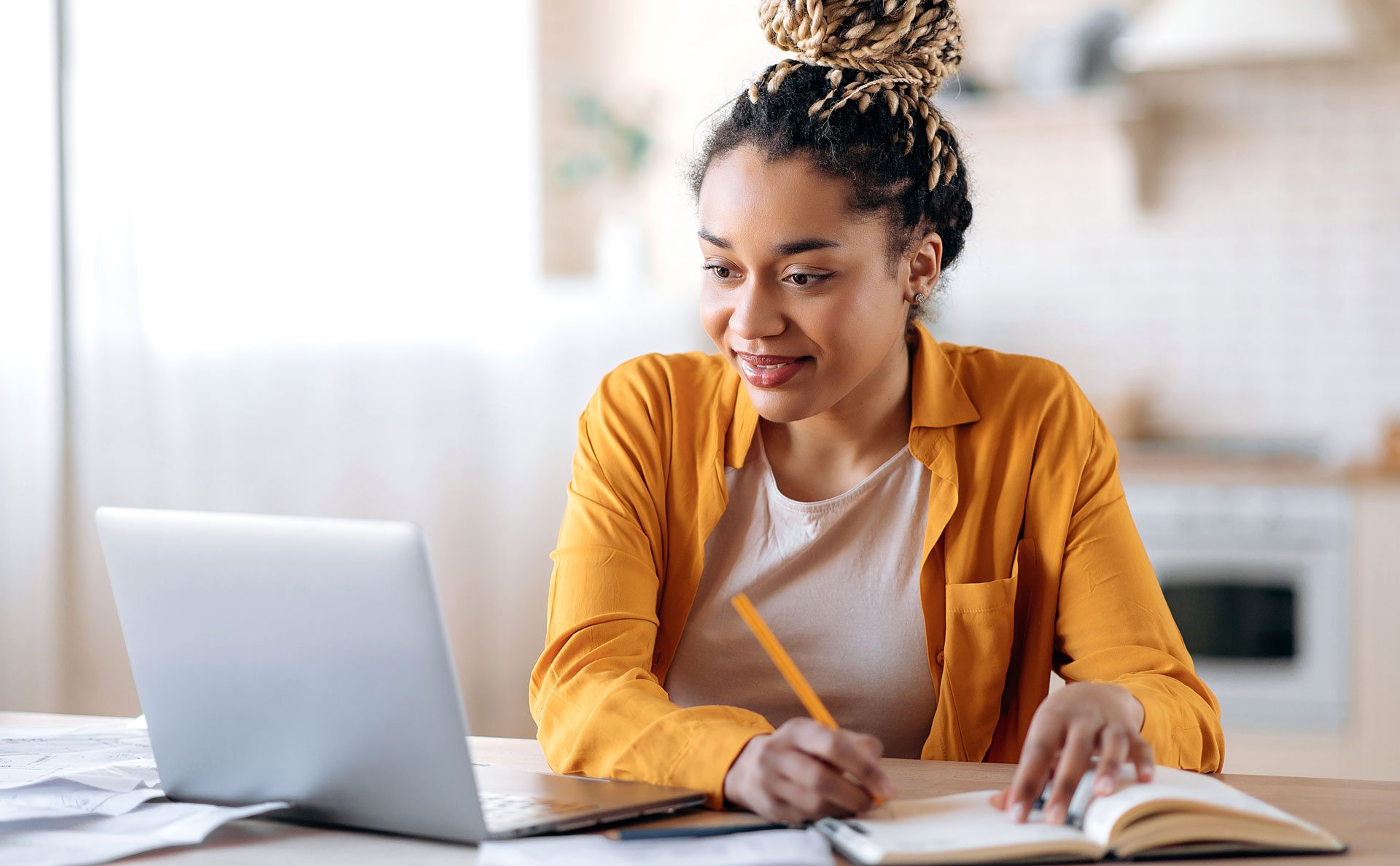 Eine Studentin sitzt vor dem Laptop und macht sich Notizen auf dem Block.