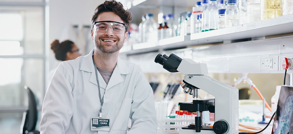 Ein Mitarbeiter sitzt im Labor uns lächelt.