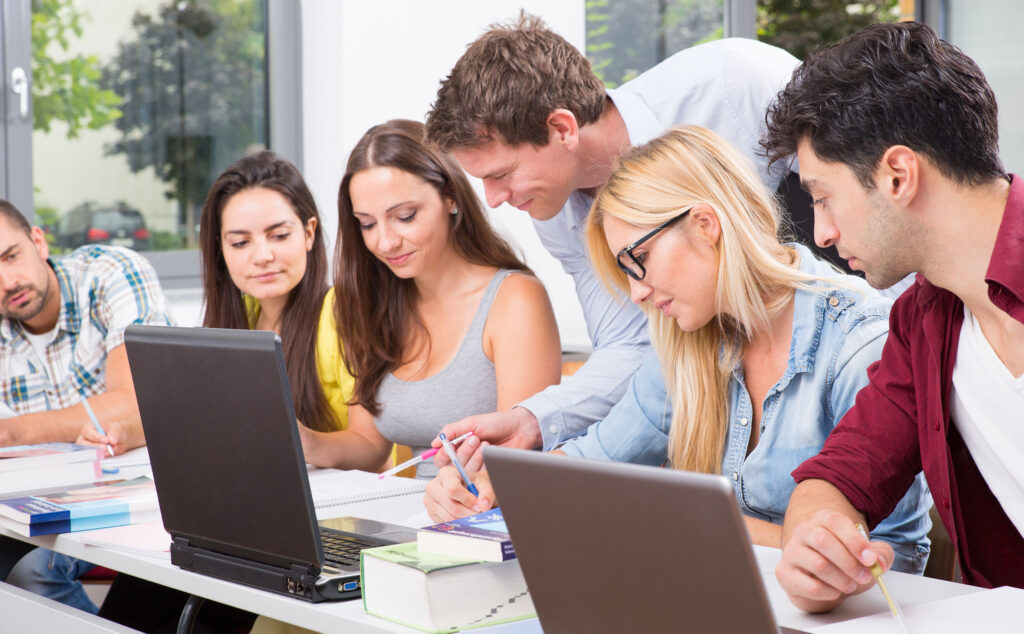 Ein Dozent hilft seinen Schülern am Laptop.