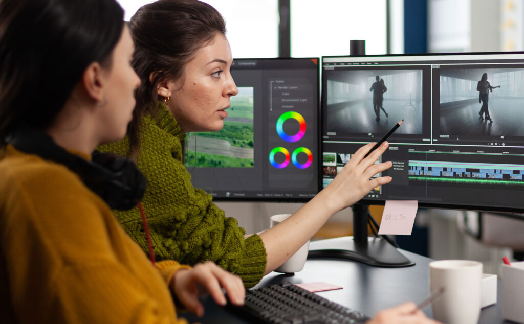 Eine Ausbilderin erklärt Ihrer Auszubildenden etwas in einem Schnittprogramm und zeigt auf den monitor.