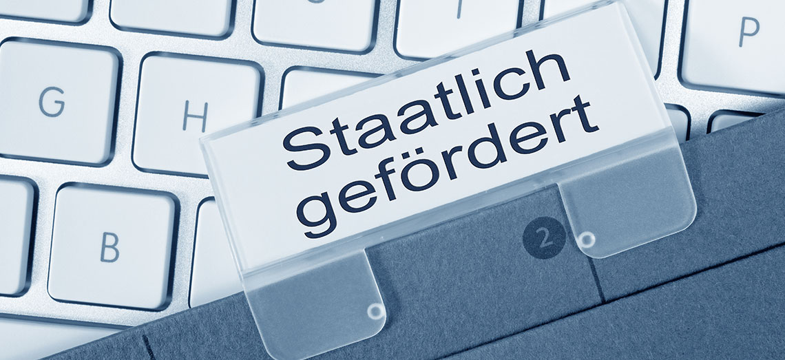 Eine Akte mit dem Reiter staatliche Förderung liegt auf einer Tastatur.