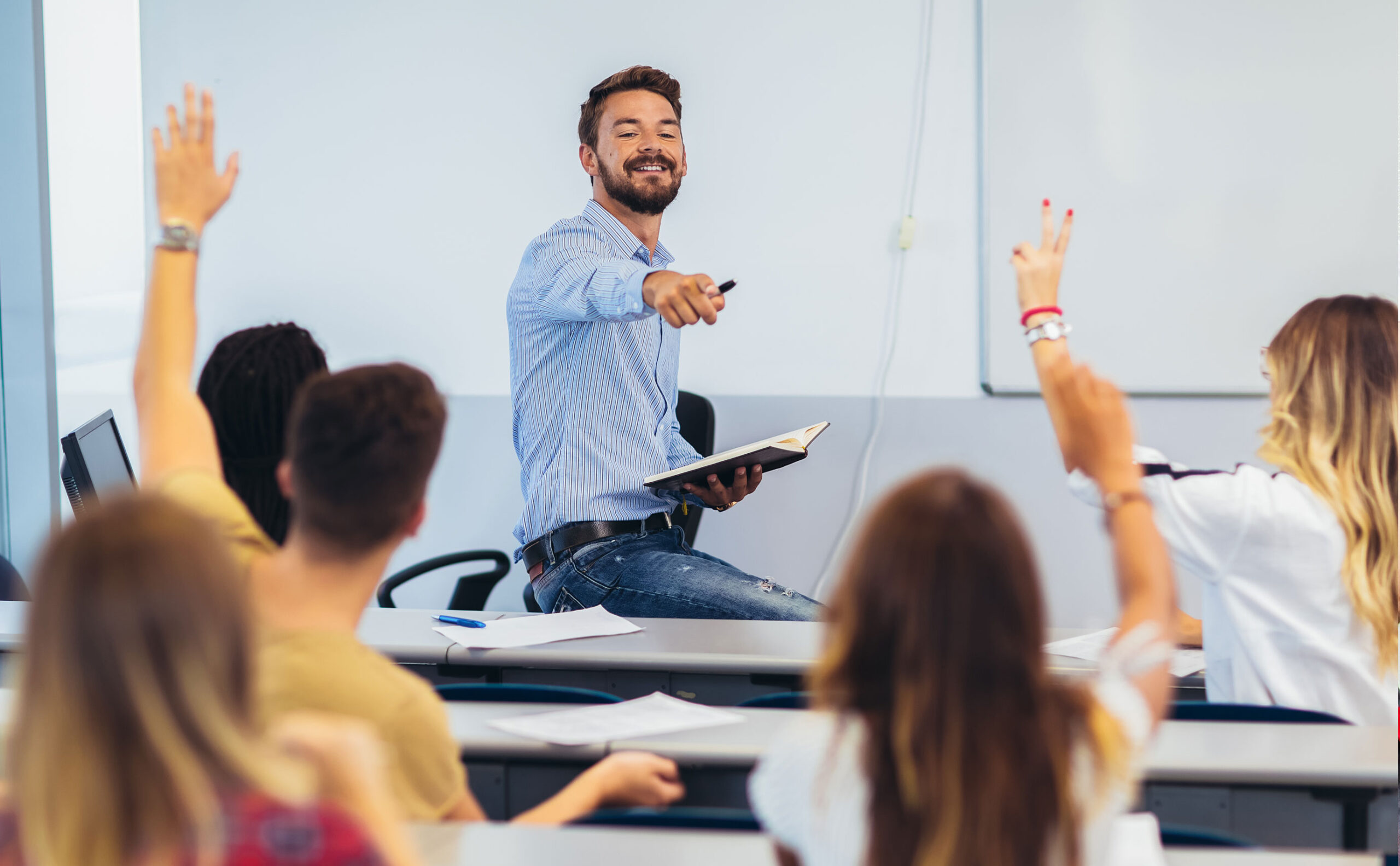 Praesenzunterricht Ein Lehrer während des Unterrichts. Er zeigt auf eine Schülerin, die sich meldet.