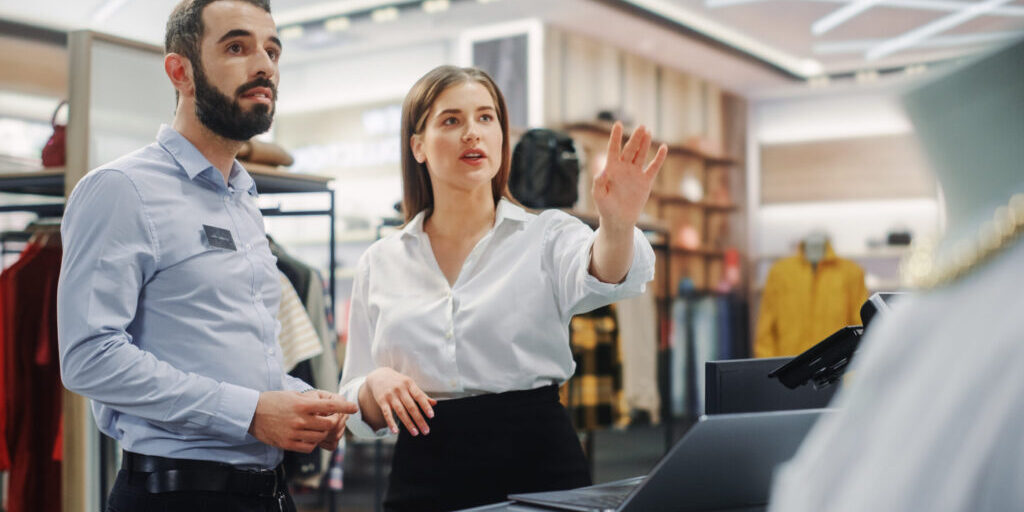 Eine Mitarbeiterin zeigt ihrem Azubi zum Handelsfachwirt etwas im Verkaufsraum.