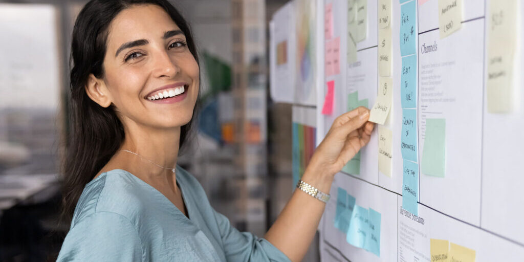 Eine Frau arbeitet an einem KANBAN-Board und lächelt.