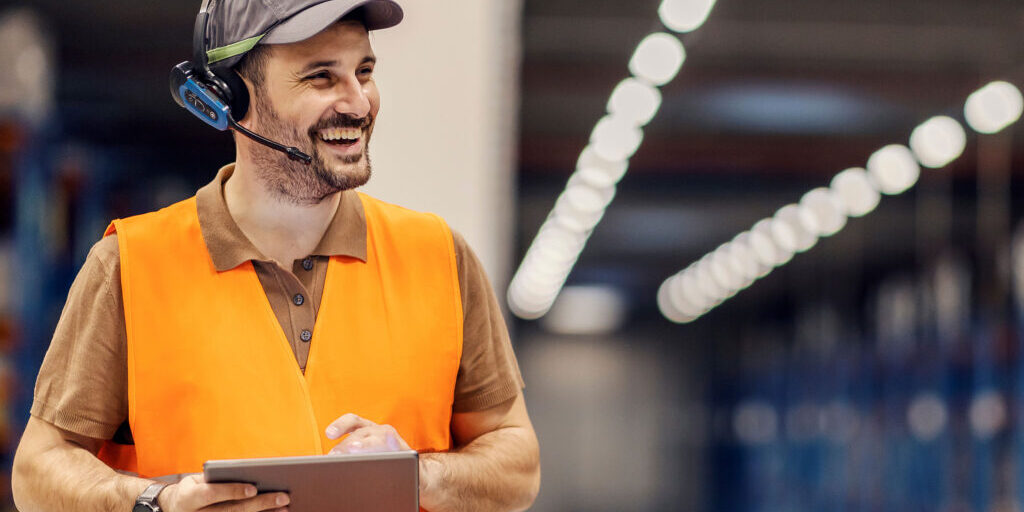 Ein Logistik-Mitarbeiter schaut auf eine Checkliste in seinen Händen und lächelt.