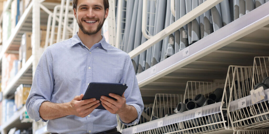 Ein Angestellter eines Baumarkts steht vor einem Regal und hält ein Notizblock in der Händen.