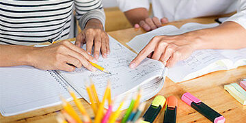 Eine Person zeigt der anderen Person etwas, das auf beschriebenen Zetteln auf einem Tisch steht.